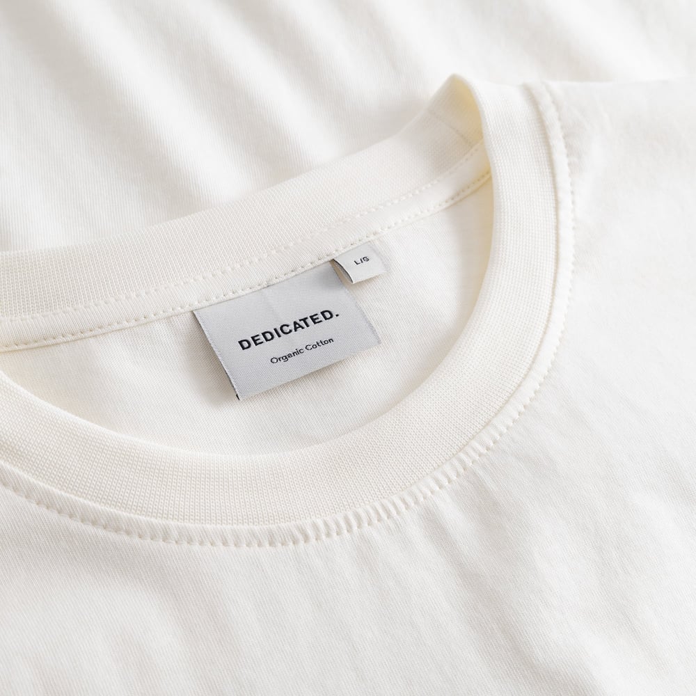 Close-up detail shot of the brand label and soft ribbed collar on the T-shirt Stockholm Karaoke Killer in off-white.