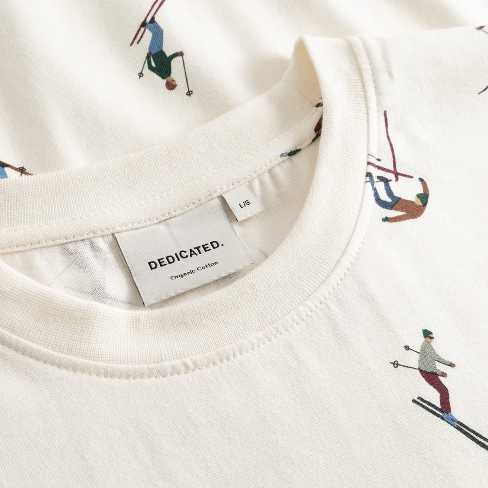 Close-up of the Dedicated Ski Team t-shirt in off-white, showing the ribbed collar and fun all-over skier print.