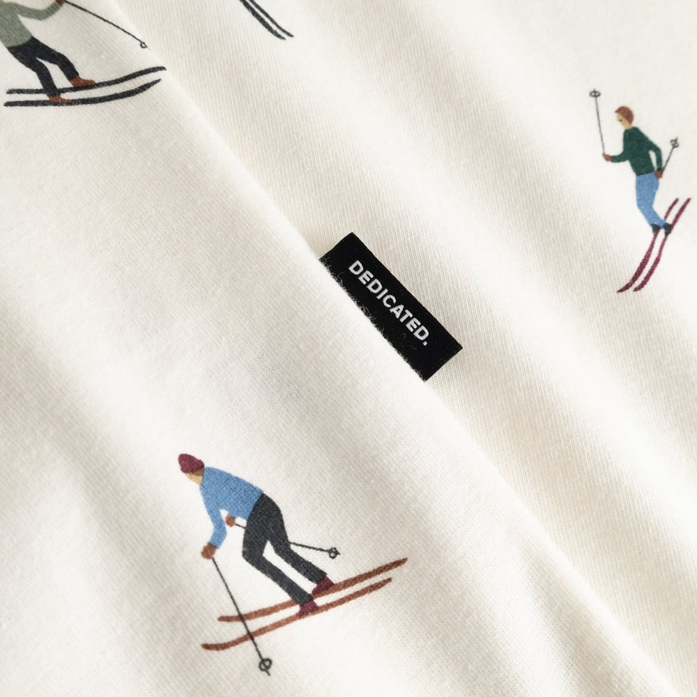 A close-up of the off-white Stockholm Ski Team t-shirt's fabric, showing the skier print and Dedicated brand tag.
