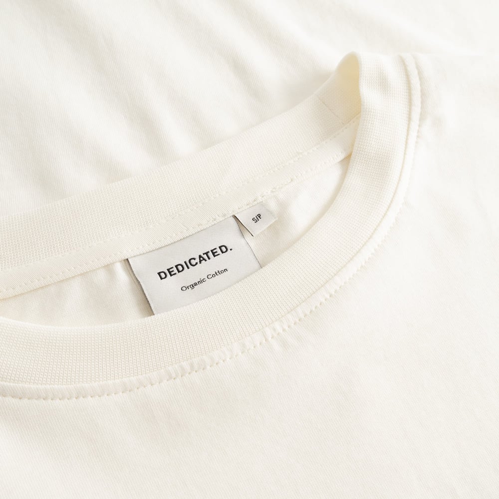 Close-up of the ribbed collar and Dedicated brand label on the off-white organic cotton T-shirt Vadstena.