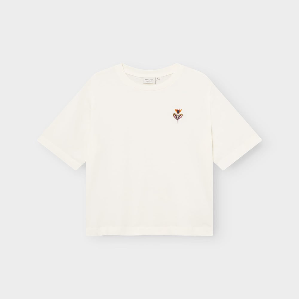 Flat lay of the off-white Vadstena t-shirt, featuring a small embroidered 'Autumn Harvest' flower on the chest.