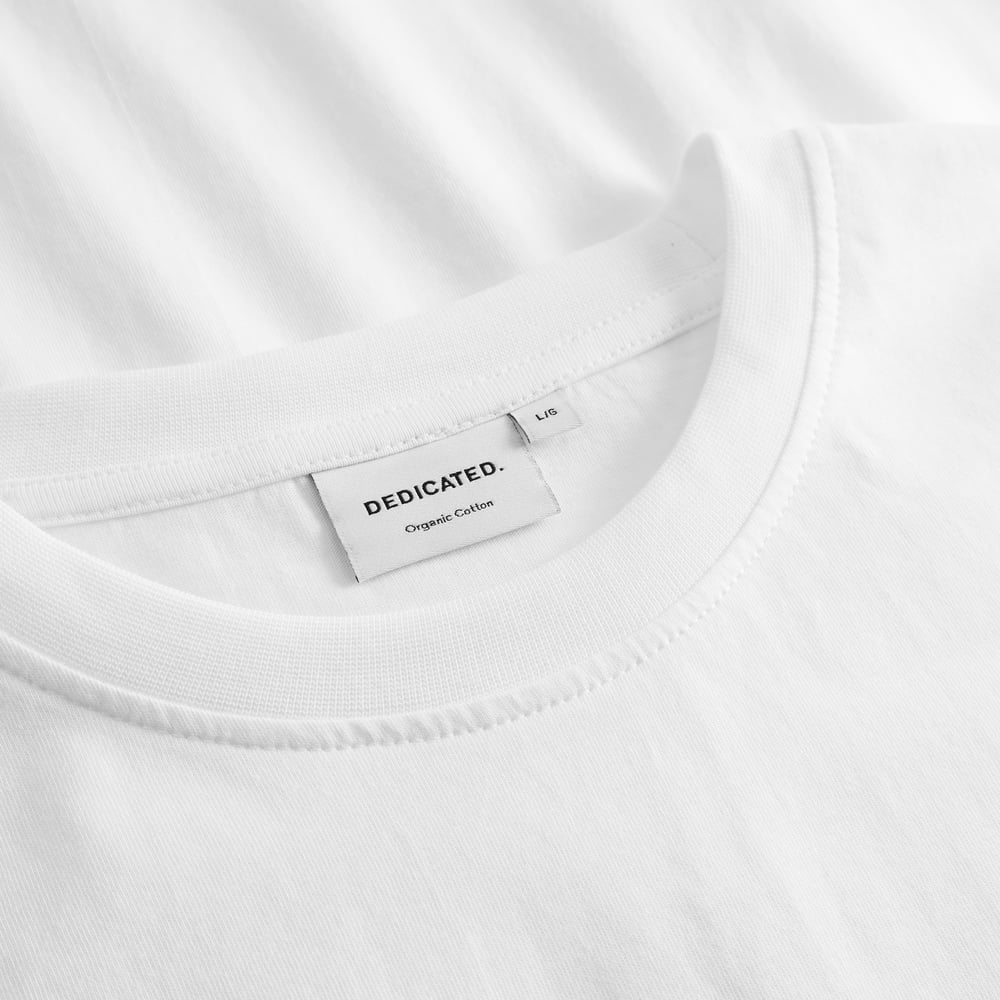 Close-up detail of the ribbed neckline and Dedicated brand label inside the white Stockholm Ski Crash EMB t-shirt.