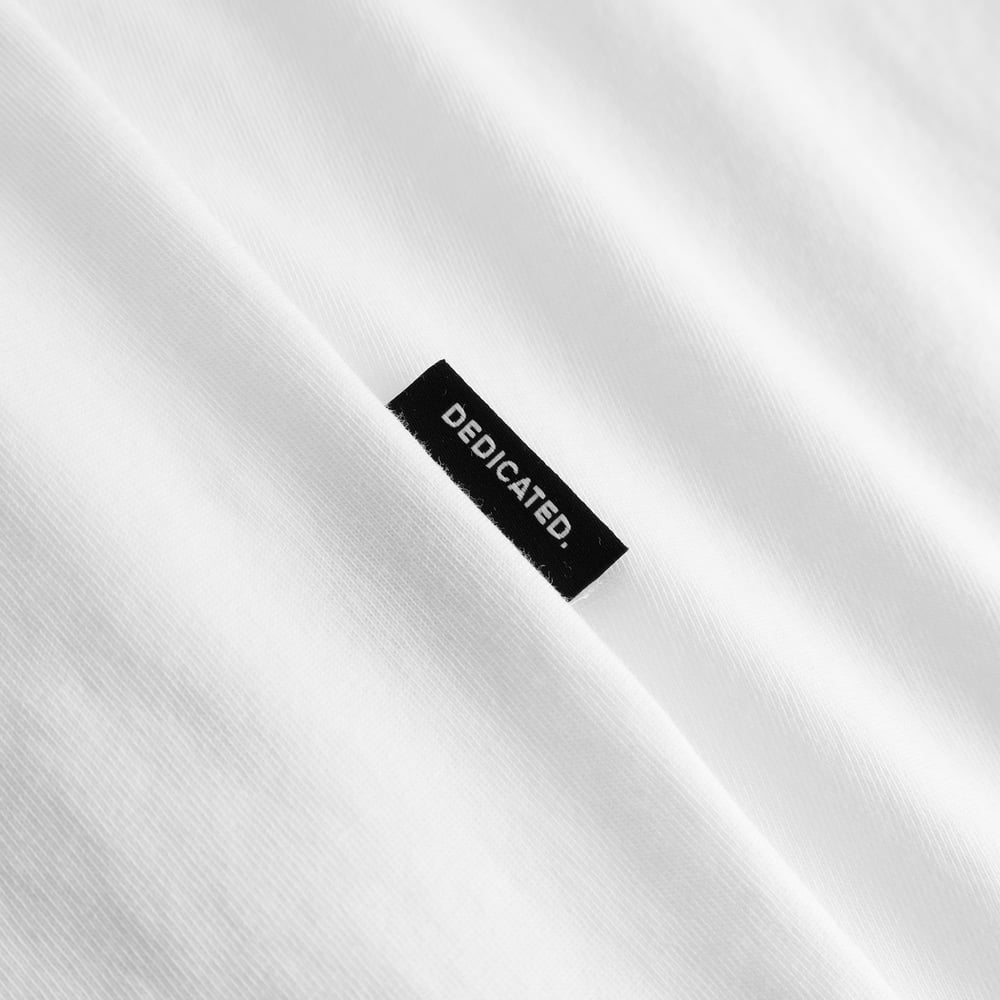 Close-up of the black Dedicated brand label on the sleeve of the white Stockholm t-shirt.