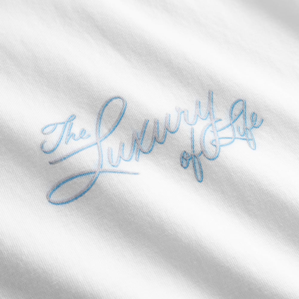 Close-up of the 'The Luxury of Life' graphic in a flowing blue script on the white Stockholm Fondue t-shirt.