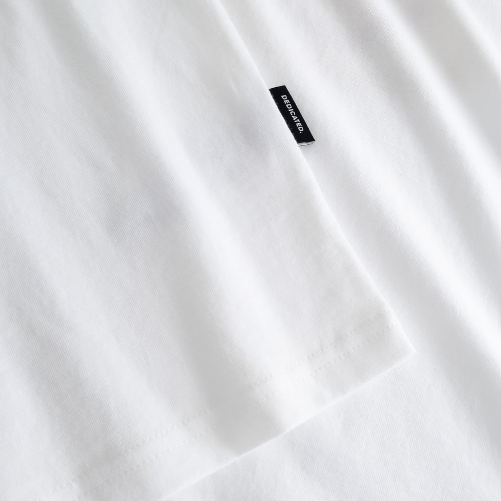 Close-up of the white T-shirt Stockholm Breakfast All Day, showing the black Dedicated brand tag on the sleeve.