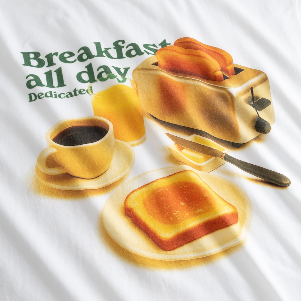 Close-up of the fun 'Breakfast all day' print on a white t-shirt, showing a retro scene with a toaster, coffee, and toast.