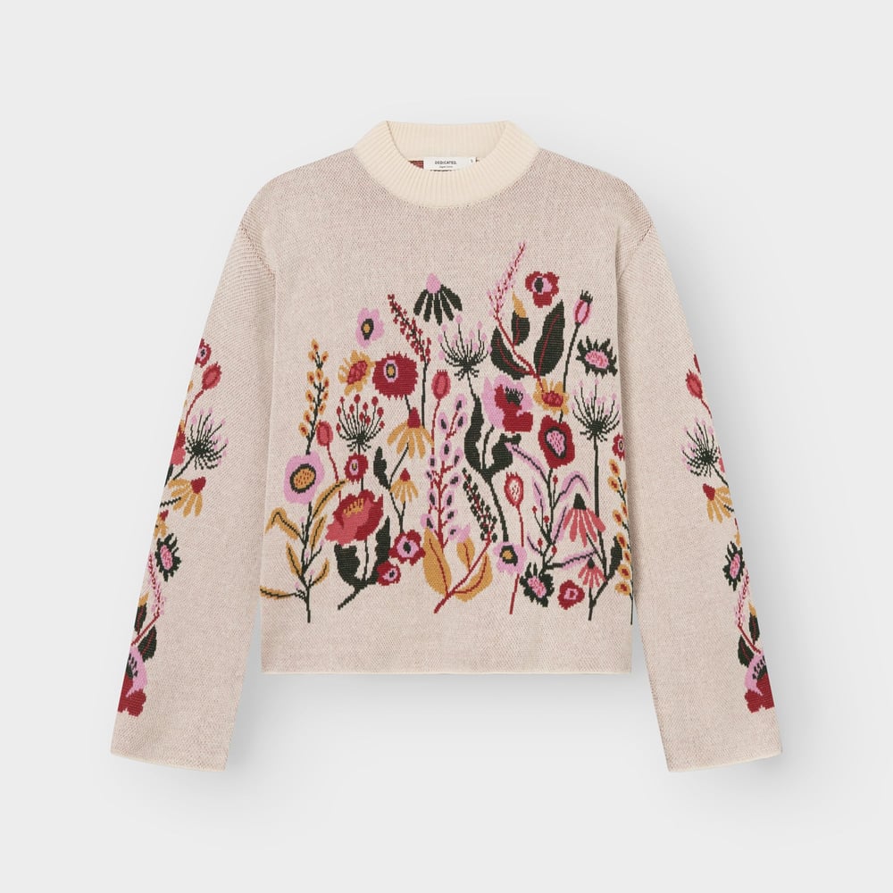 A flat lay of the vanilla white Limhamn sweater, featuring a beautiful jacquard knit pattern of colorful folk flowers.