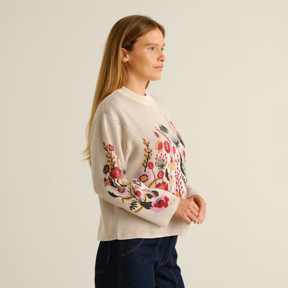 Side profile of a woman wearing the vanilla Sweater Limhamn, featuring a vibrant folk flower design on the body and sleeve.