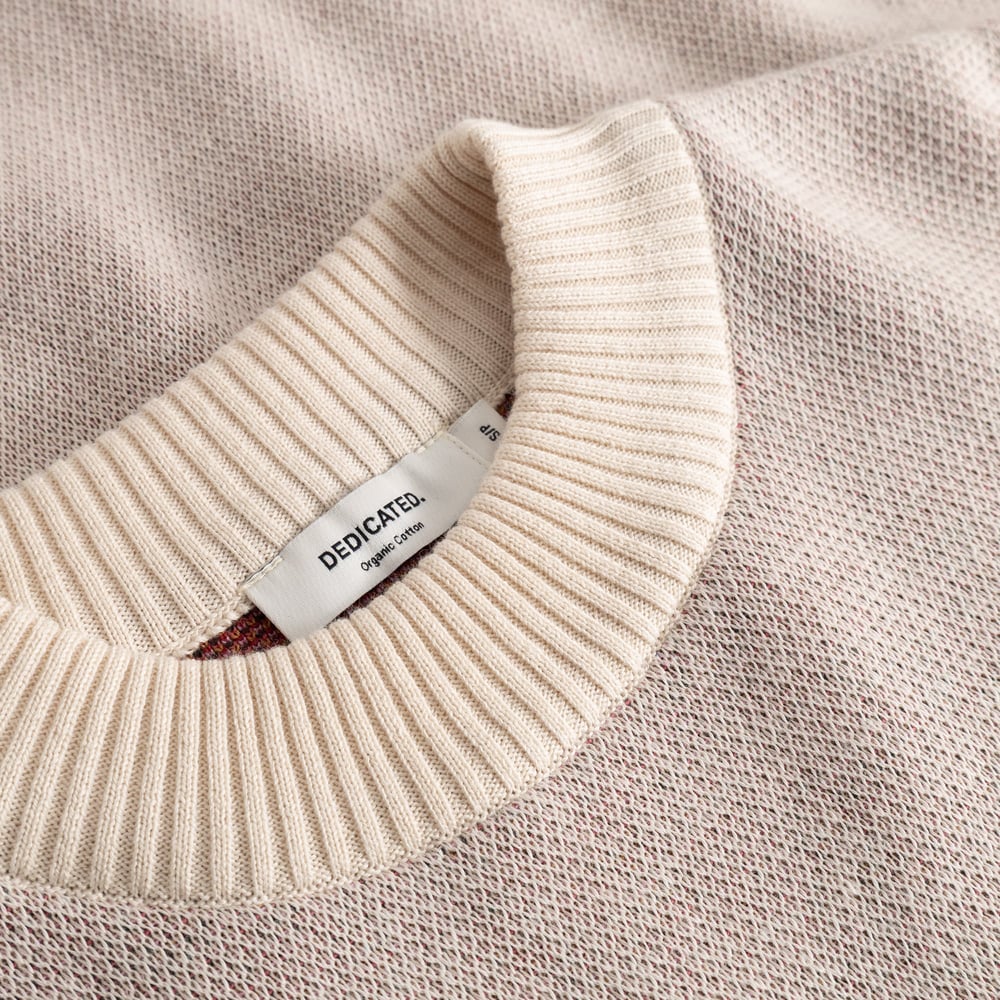 Close-up on the soft ribbed collar and jacquard knit of the vanilla white Limhamn sweater, featuring the Dedicated label.