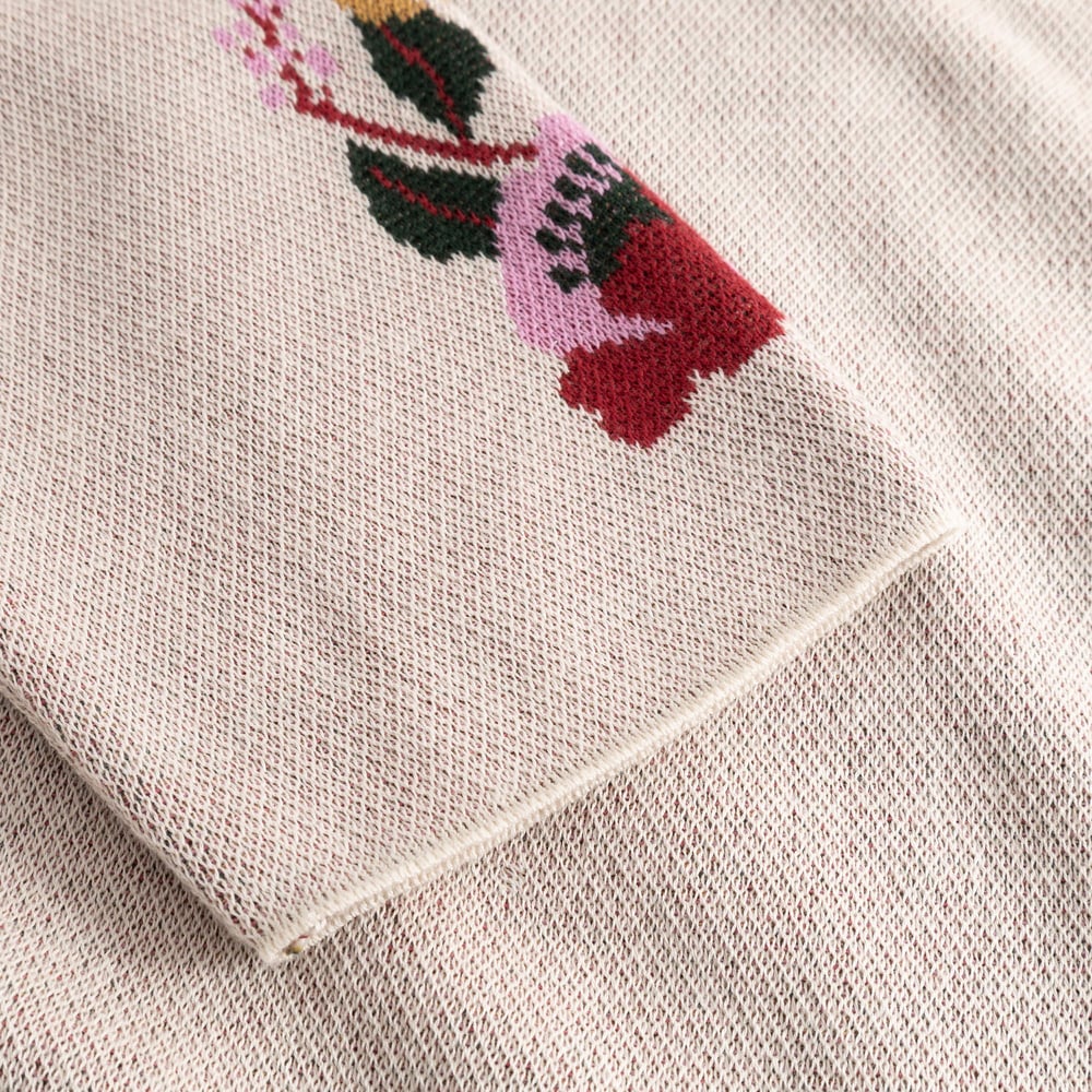 A close-up of the vanilla white Sweater Limhamn, detailing the colourful jacquard-knit folk flower on the sleeve.