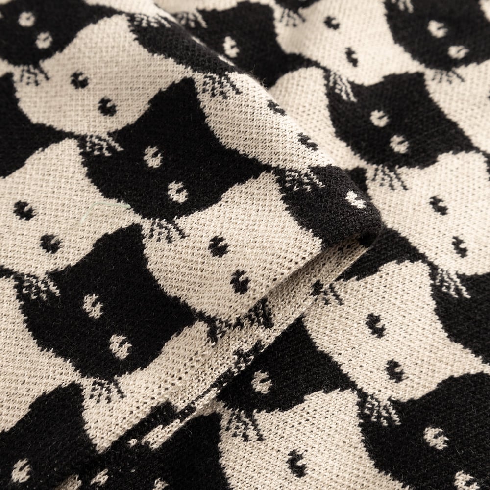 A close-up view of the Scarf Rossberga, showcasing the fine jacquard knit and the playful Pepita Cats pattern in oat white.