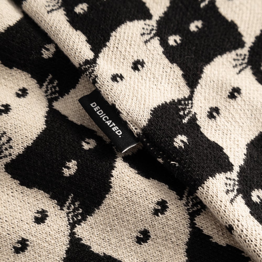 Detailed view of the Scarf Rossberga's jacquard knit, featuring a black and oat white cat pattern and the Dedicated logo tag.
