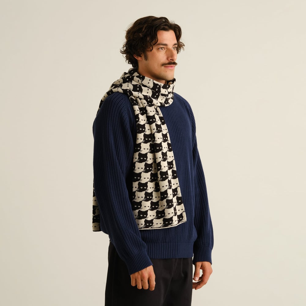 Model wearing the Scarf Rossberga Pepita Cats, wrapped snugly over a navy blue knit sweater against an off-white background.
