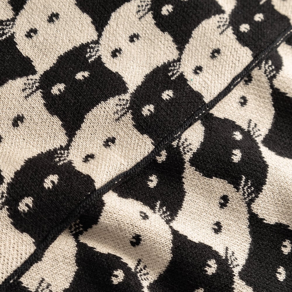 A close-up of the jacquard knit Scarf Rossberga, showing the playful cat pattern in oat white and black.