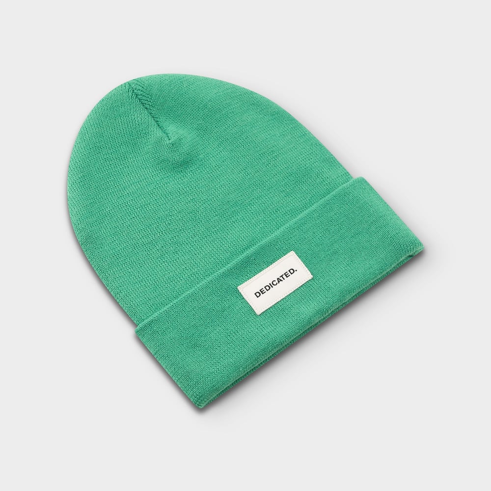 Dedicated Beanie Kiruna i Winter Green, plattlagd i en studiobild. Mössan har ett brett uppvik med en logotyp.