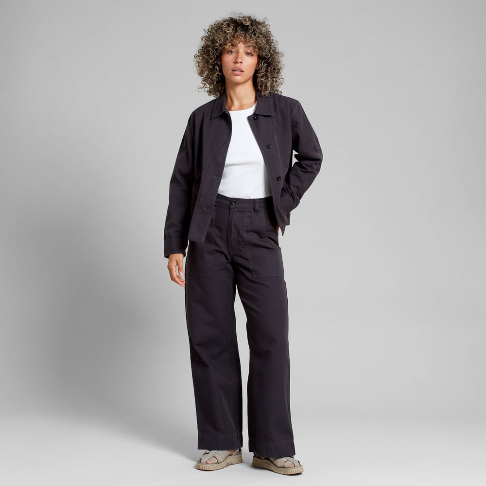 Model wears the black Stiby Canvas jacket with matching wide-leg trousers, a white top, and sandals, on a grey background.