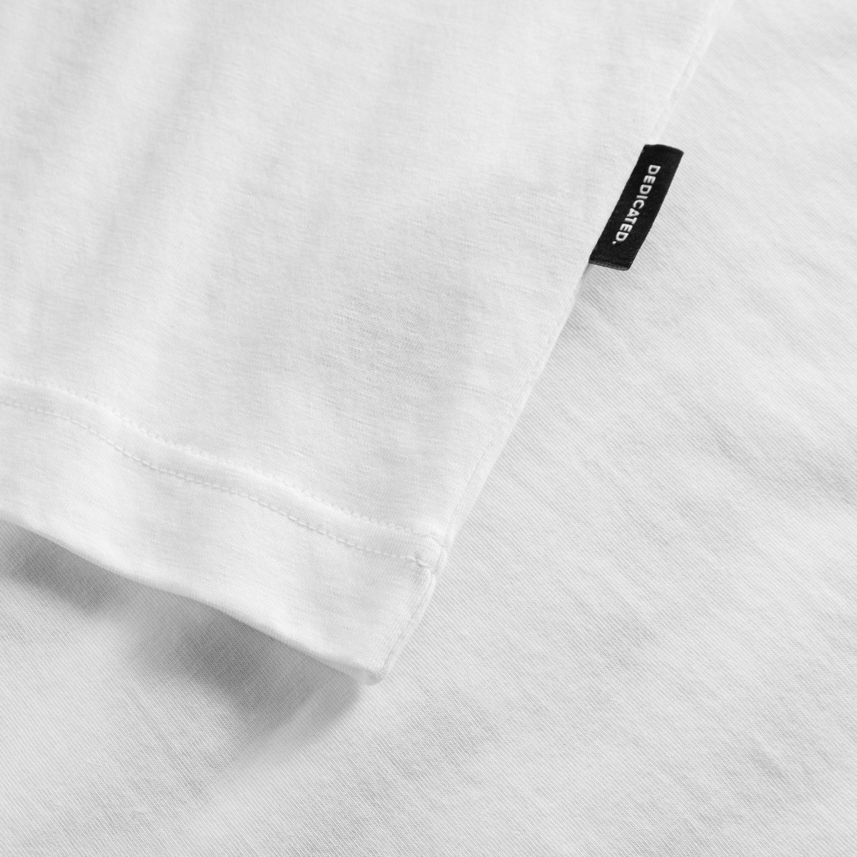 Close-up of the T-shirt Vadstena Dancing Man in white, showing the fabric, sleeve hem and small black Dedicated brand tag.