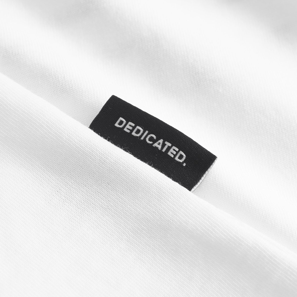 Close-up of the signature black Dedicated label, a mark of quality on the off-white Stockholm Beach Habitat t-shirt.