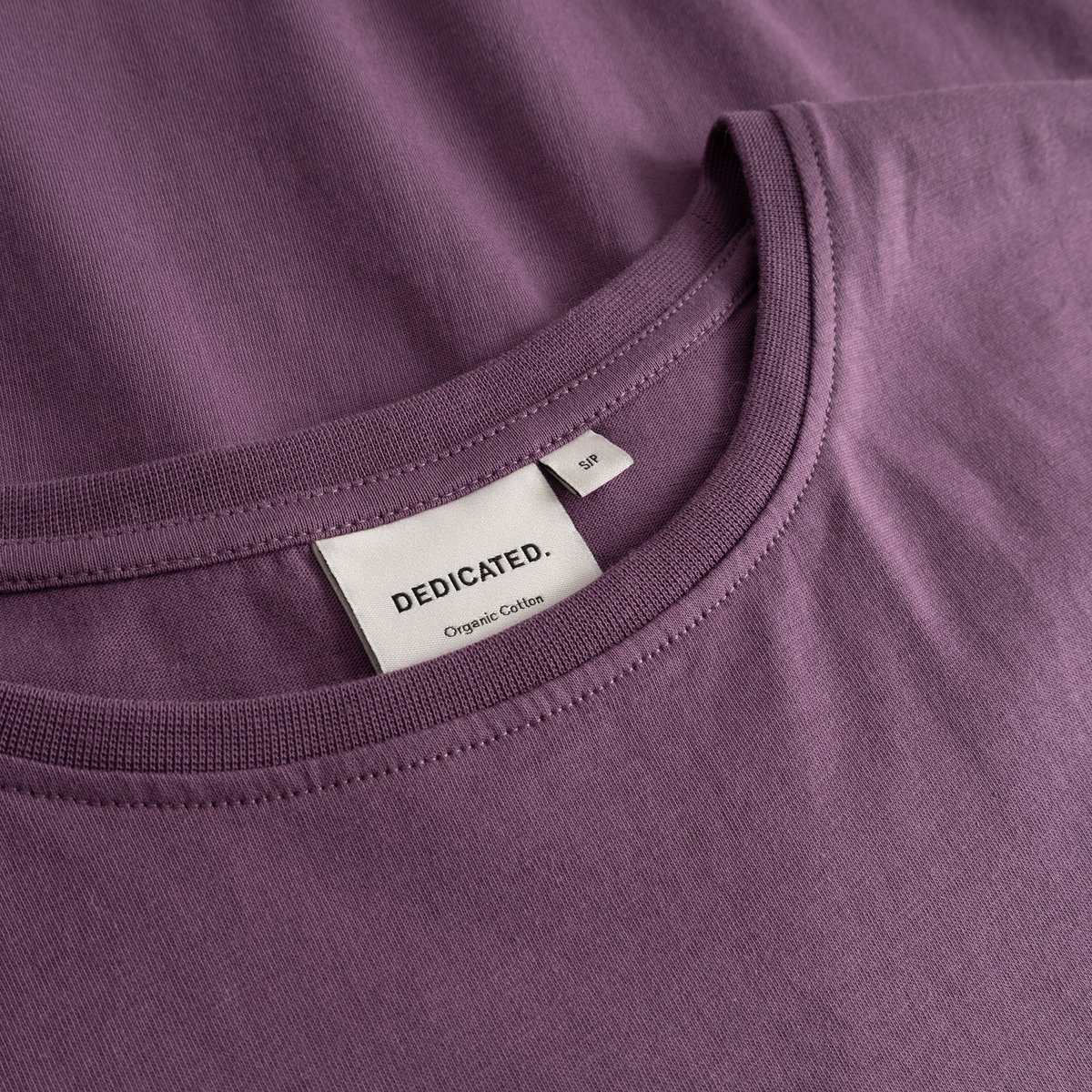 A detailed close-up of the ribbed crew neck collar and brand label on the berry purple T-shirt Visby.
