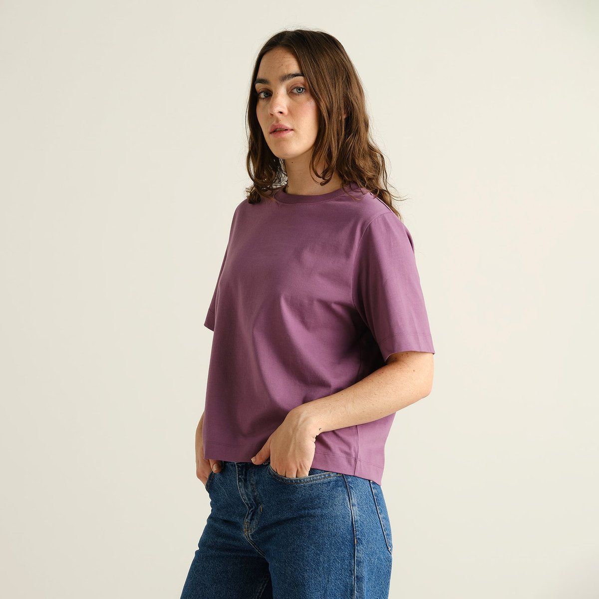 A woman models the T-shirt Vadstena Base in Berry Purple, paired with blue jeans for a cool and casual look.