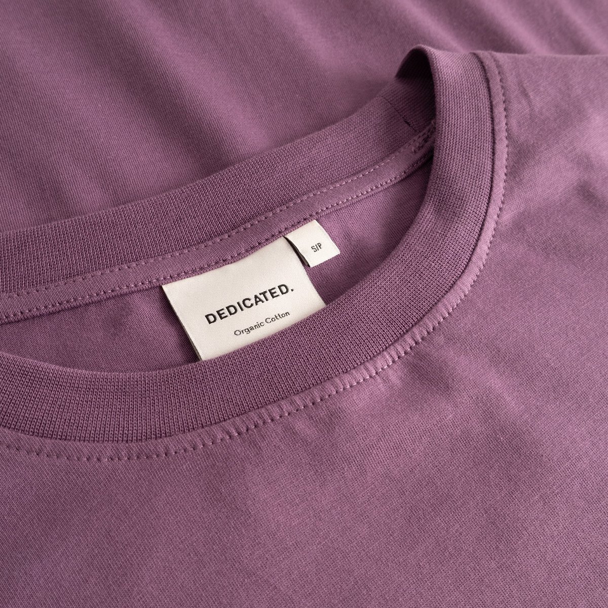 Detail shot of the organic cotton T-shirt Vadstena Base in Berry Purple, showing the soft ribbed collar and brand label.