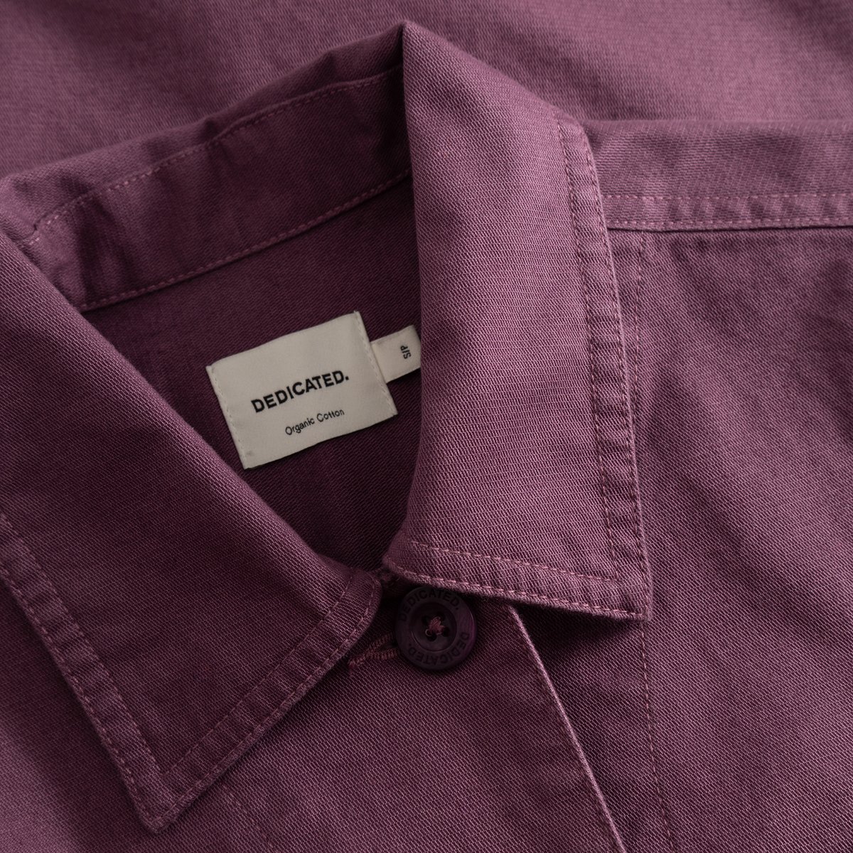 Detaljbild av kragen, tyget och märkesetiketten på jackan Stiby Berry Purple.