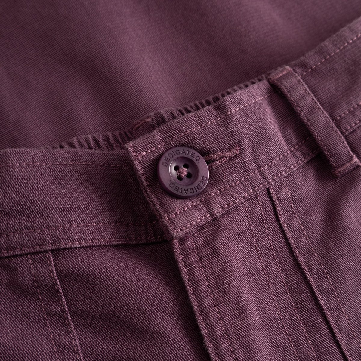 Detaljbild på Workwear Pants Vara i Berry Purple som visar dobby ripstop-tyget och den specialdesignade Dedicated-knappen.