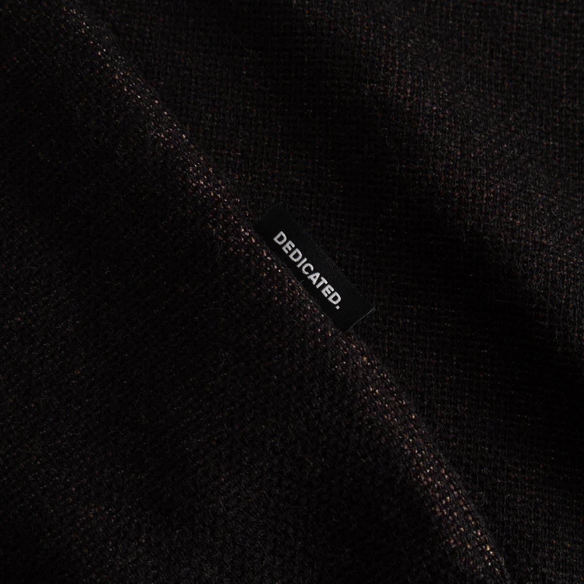 Close-up detail of the Sweater Arendal Long Cat in black, showcasing the jacquard knit texture and the Dedicated brand label.