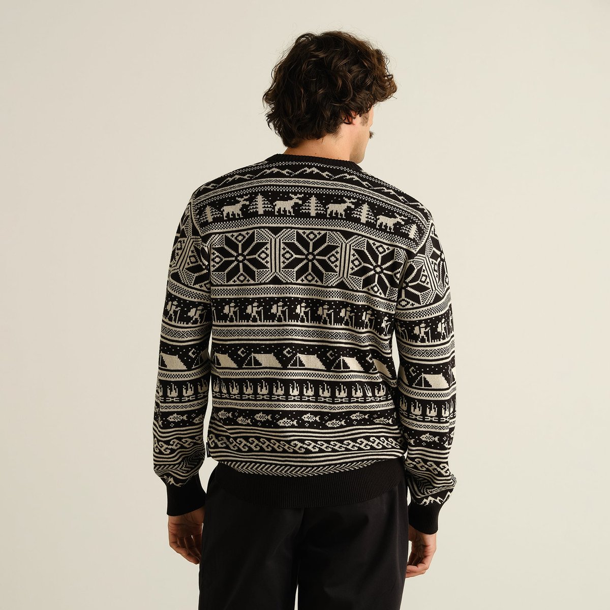 Model from the back wearing the black Sweater Mora Fairisle Hike, showing off its unique pattern of hikers, moose, and tents.
