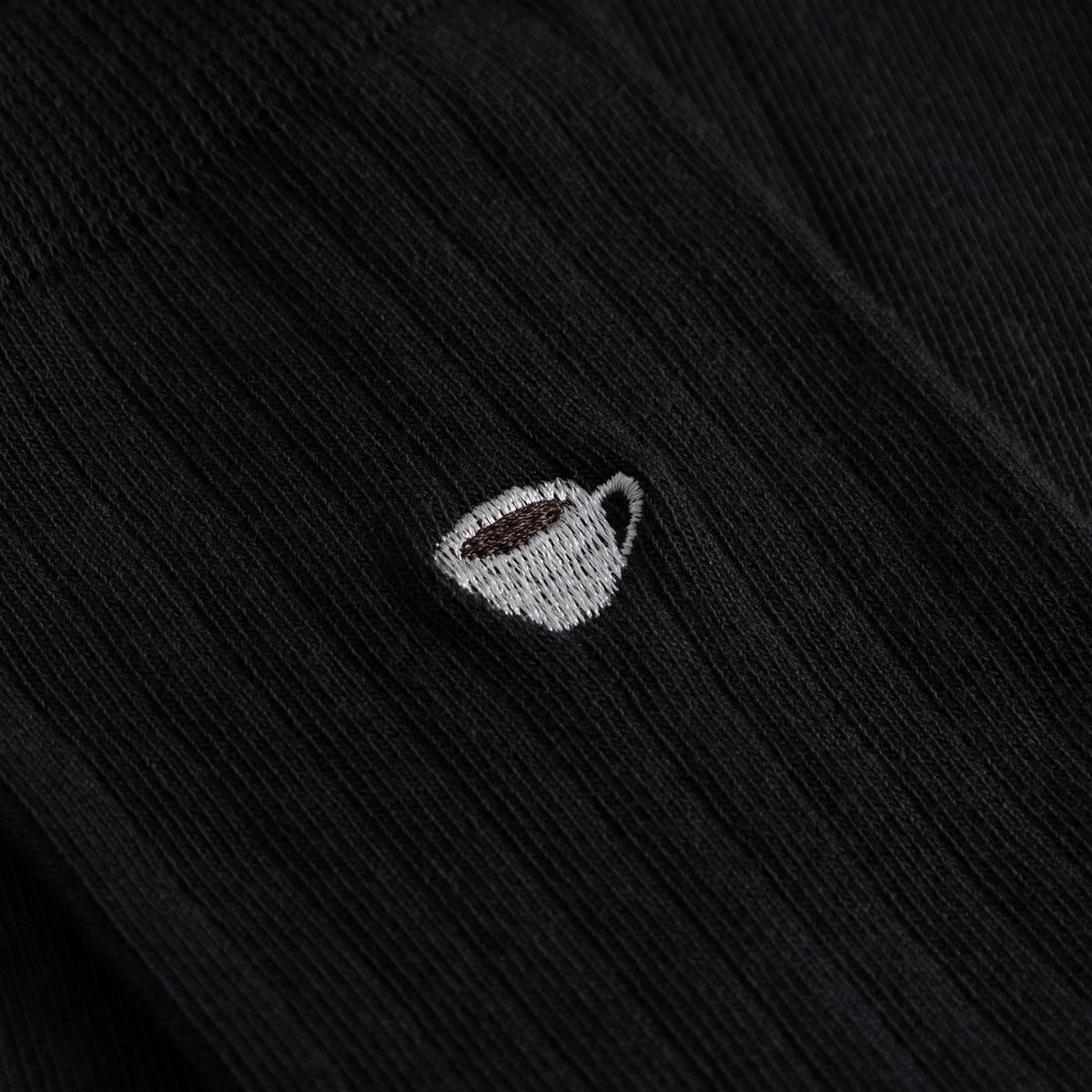 Close-up of the charming coffee cup embroidery on the black ribbed Knivsta socks.