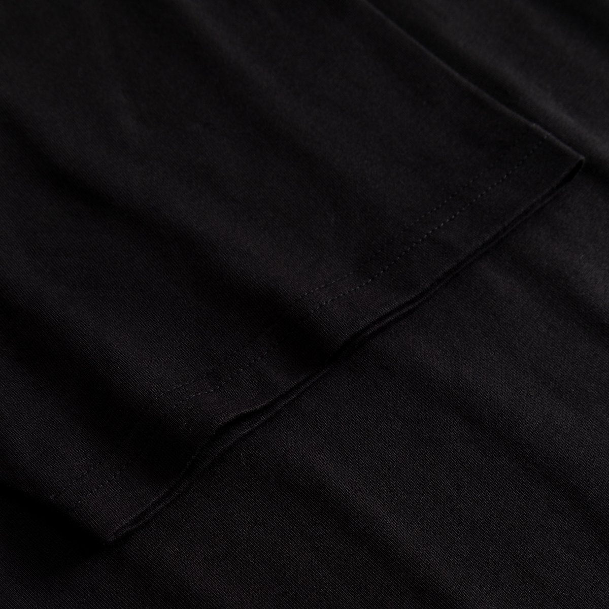 A close-up of the sleeve and stitching detail on the black T-shirt Stockholm Worship Coffee.