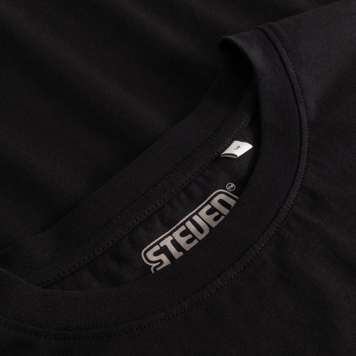 Close-up of the ribbed collar and the printed Steven Rhodes logo inside the black T-shirt Vadstena.