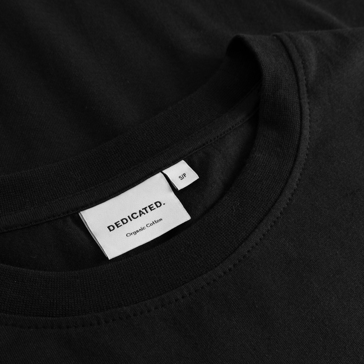 Close-up of the Dedicated brand label and ribbed neckline on the black organic cotton T-shirt Vadstena Autumn Harvest.