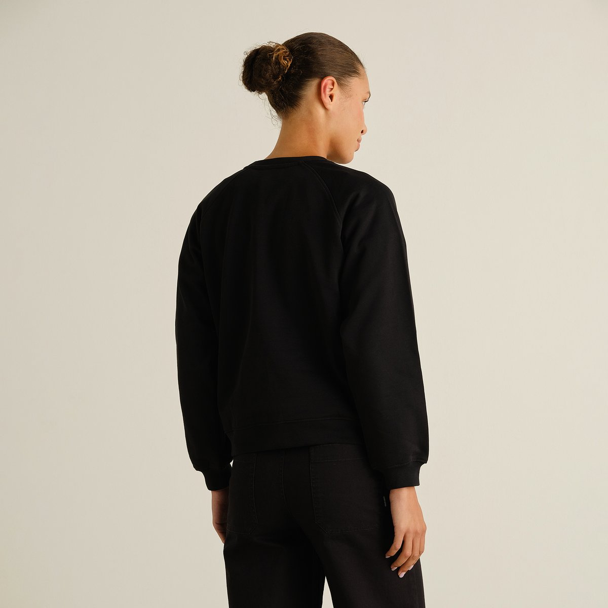 A model wearing the black Sweatshirt Ystad Painted Swans, seen from the back to showcase the fit and raglan sleeves.
