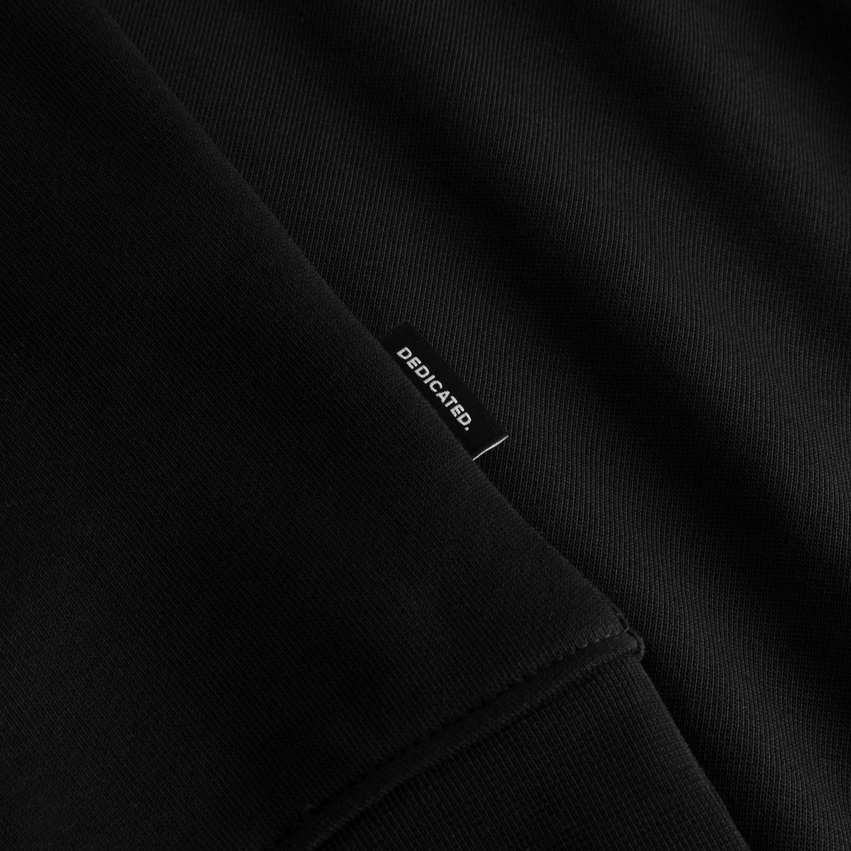 Close-up detail of the Sweatshirt Ystad Painted Swans in black, highlighting the small Dedicated brand tag.