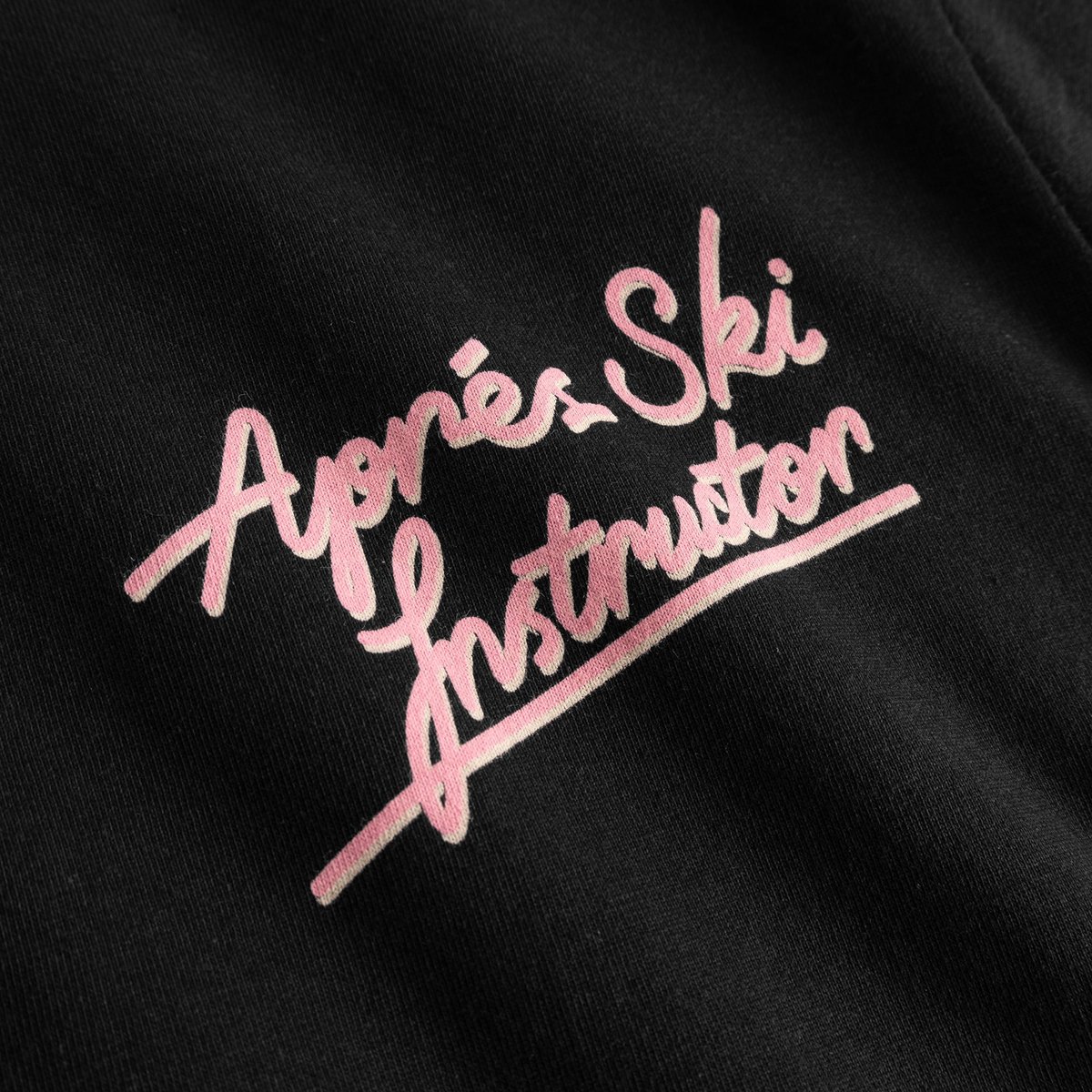 Close-up of the pink 'Après Ski Instructor' print in a fun, retro script on the black Stockholm T-shirt.