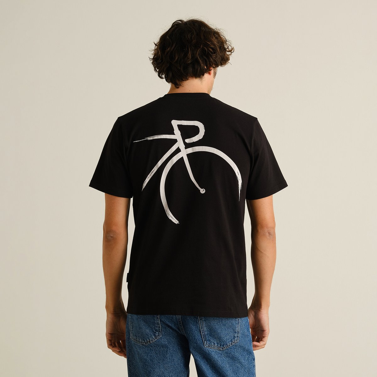 A guy showing off the back of the black T-shirt Stockholm, featuring a cool, painted-style bicycle graphic.