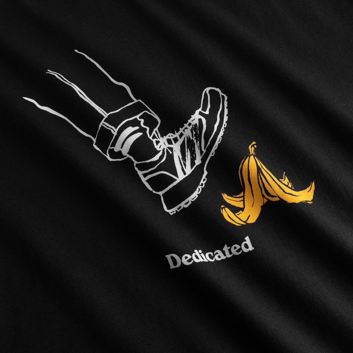 Lustiger Print auf dem T-Shirt Stockholm Life Black in Nahaufnahme: ein Fuß rutscht gleich auf einer Bananenschale aus.