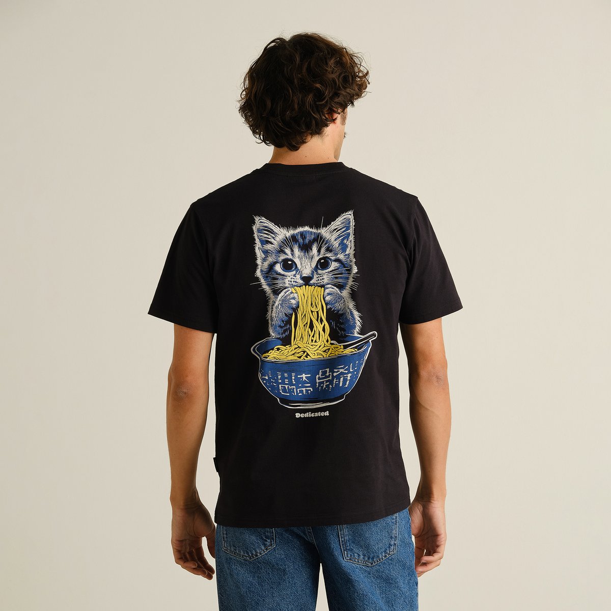 A model seen from the back wearing the black T-shirt Stockholm with a large, playful print of a kitten eating noodles.
