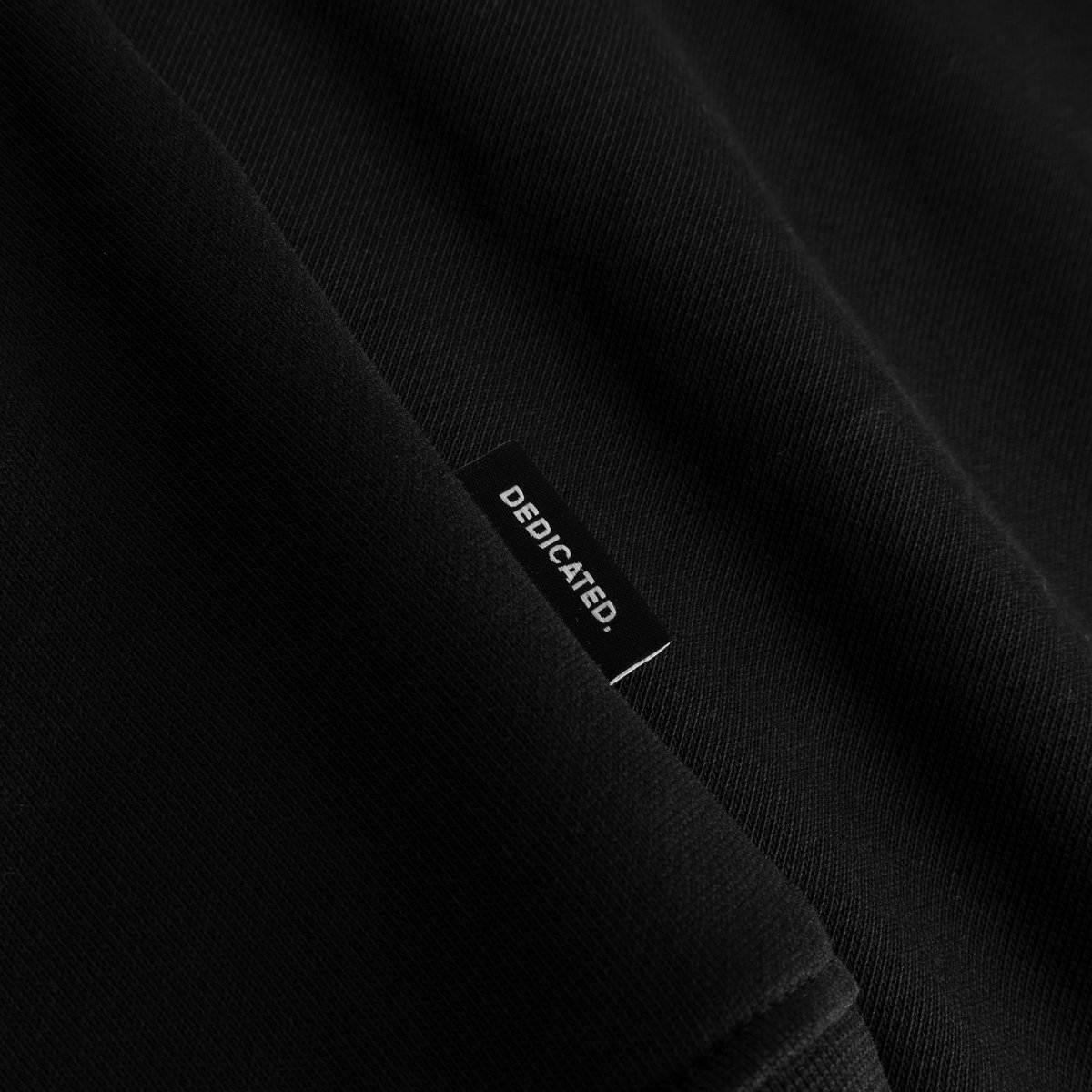 Close-up of the DEDICATED label on the hem of the soft, black organic cotton Sweatshirt Malmoe Perch.