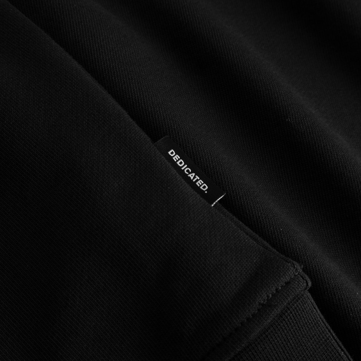 Close-up of the Dedicated brand label on the seam of the black Sweatshirt Malmoe Apres Ski Instructor.