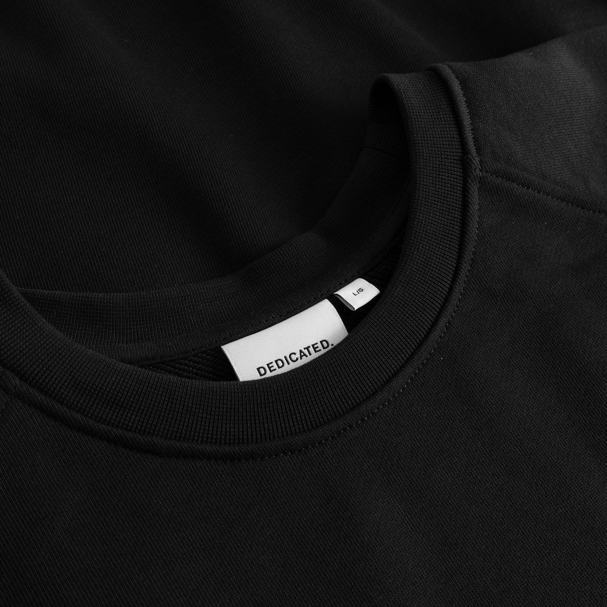 Close-up of the classic black Malmoe sweatshirt, showing the ribbed collar and the crisp white Dedicated brand label.