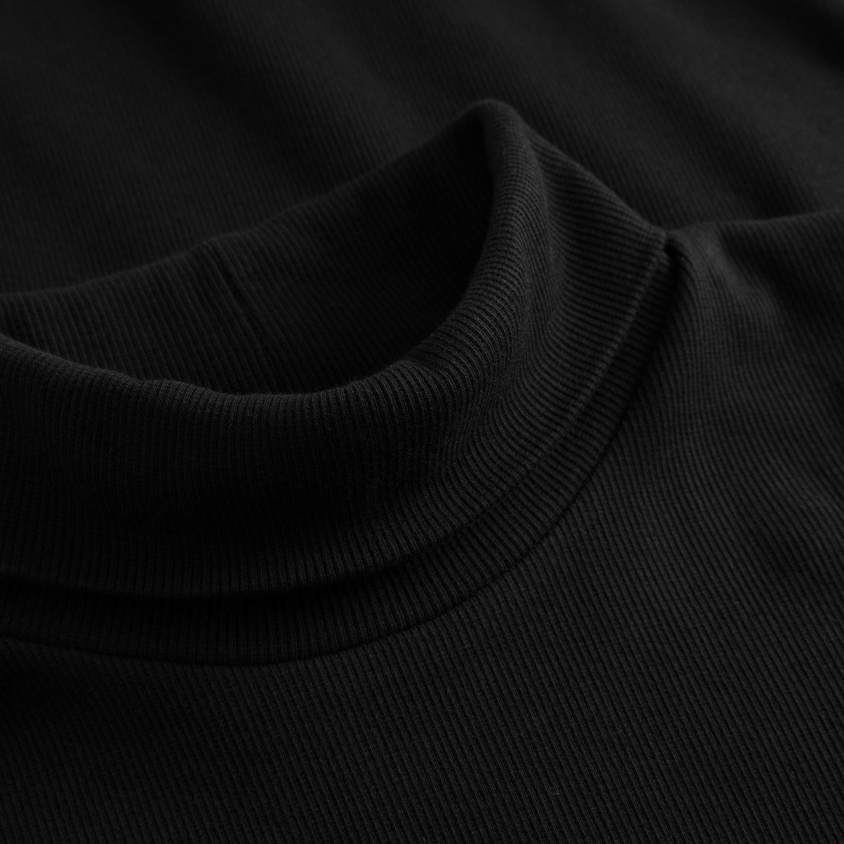 Detailansicht des umklappbaren Rollkragens des schwarzen Rippkleids Lunsen aus weichem 2x2-Rippstoff.