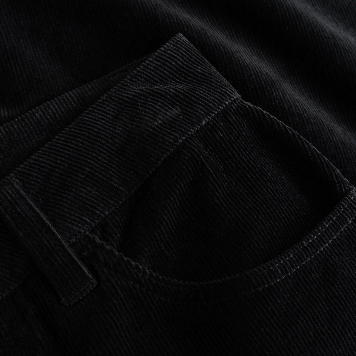 Eine Detailaufnahme der schwarzen Cordhose Ryda, die die Textur des Stoffes und die Vordertasche hervorhebt.