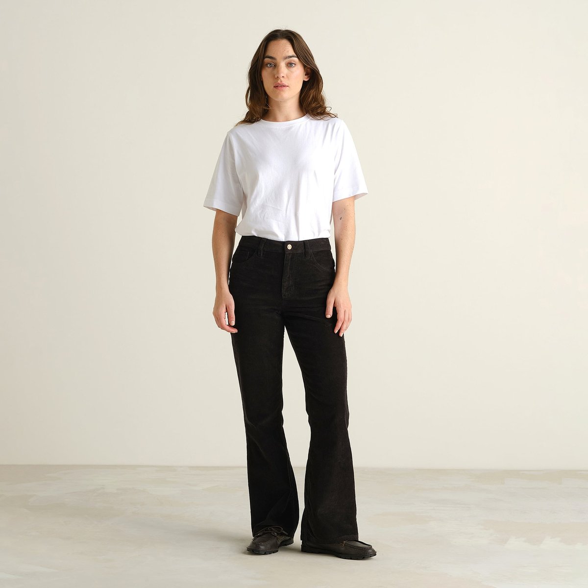 Model in Frontalansicht trägt die schwarze Cordhose Ryda im Bootcut-Stil zu einem weißen T-Shirt.