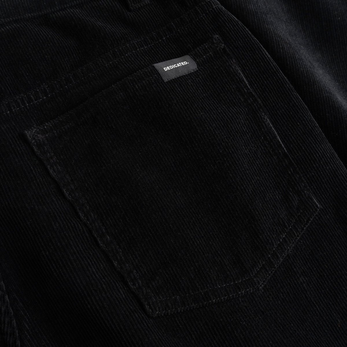 Nahaufnahme der Gesäßtasche der schwarzen Cordhose Ryda. Zu sehen sind die Cordstruktur und das kleine Dedicated-Markenlabel.