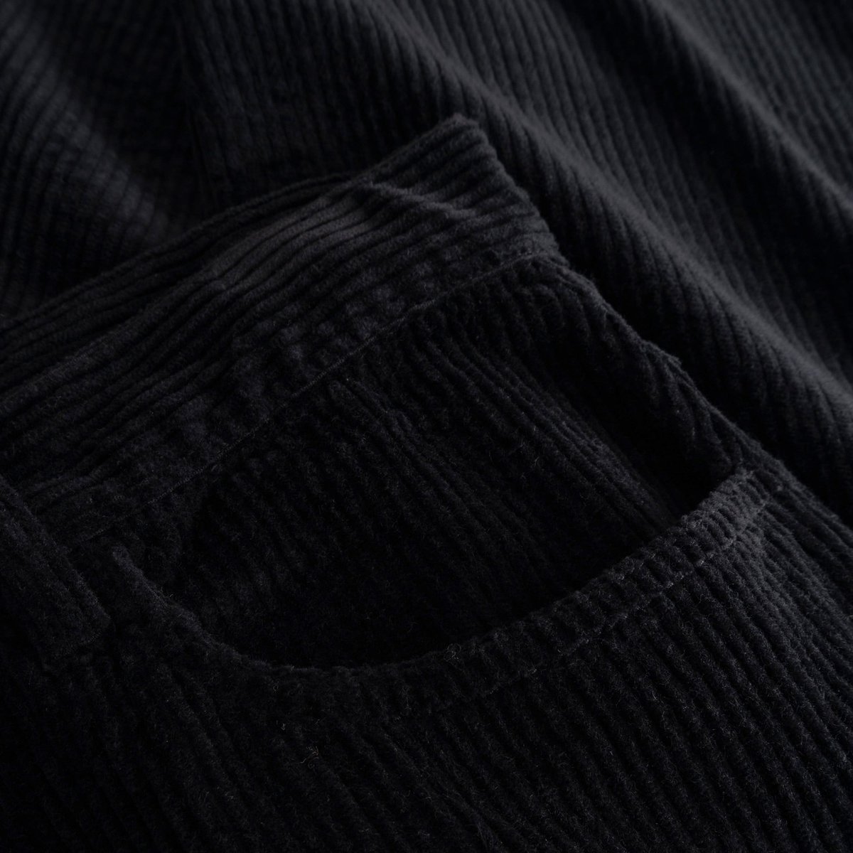A close-up view of the rich, ribbed corduroy fabric and front pocket of the black Hamburg pants.