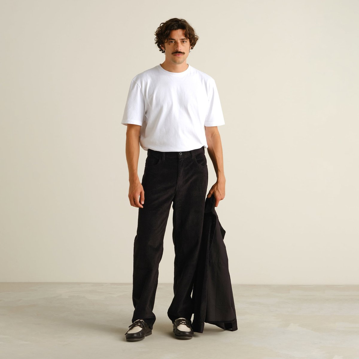 Male model wearing the black Hamburg Corduroy Pants with a white t-shirt, holding a matching black jacket.