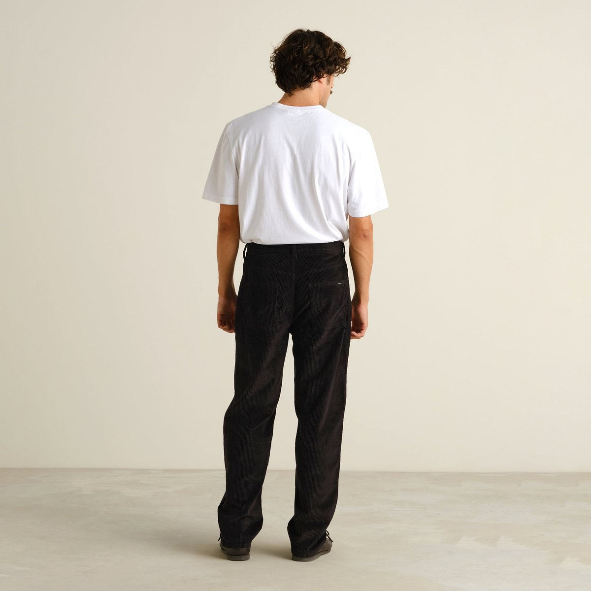 Back view of a model wearing the relaxed-fit Hamburg Corduroy Pants in black with a white t-shirt.