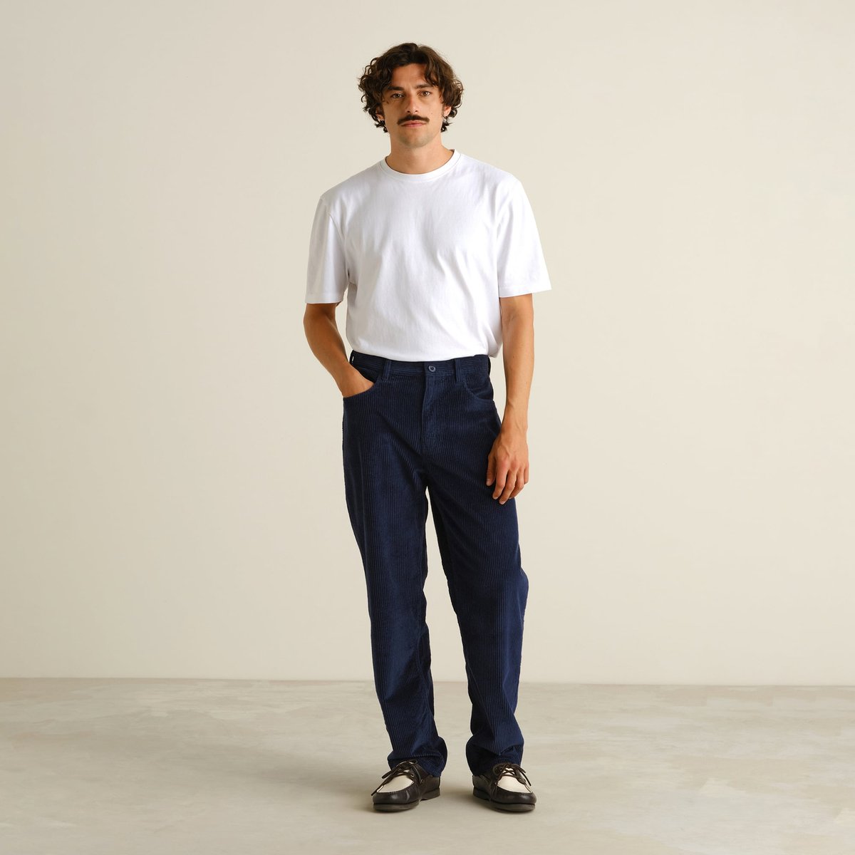 Full-length shot of a model wearing the relaxed-fit Hamburg Corduroy Pants in navy with a classic white t-shirt.